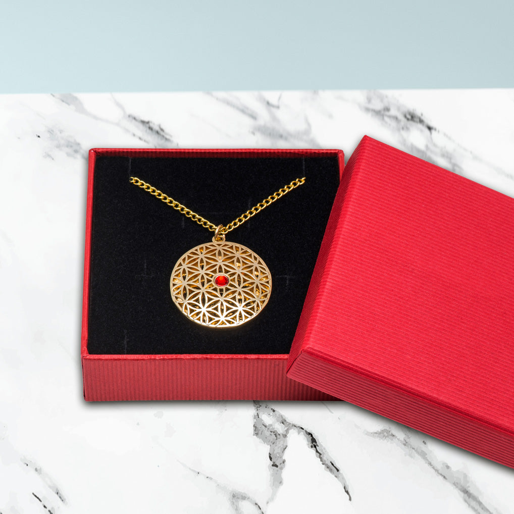 Der Anhänger Blume des Lebens mit rotem Stein wird mit einer Gliederkette in einem Schmuckkästchen